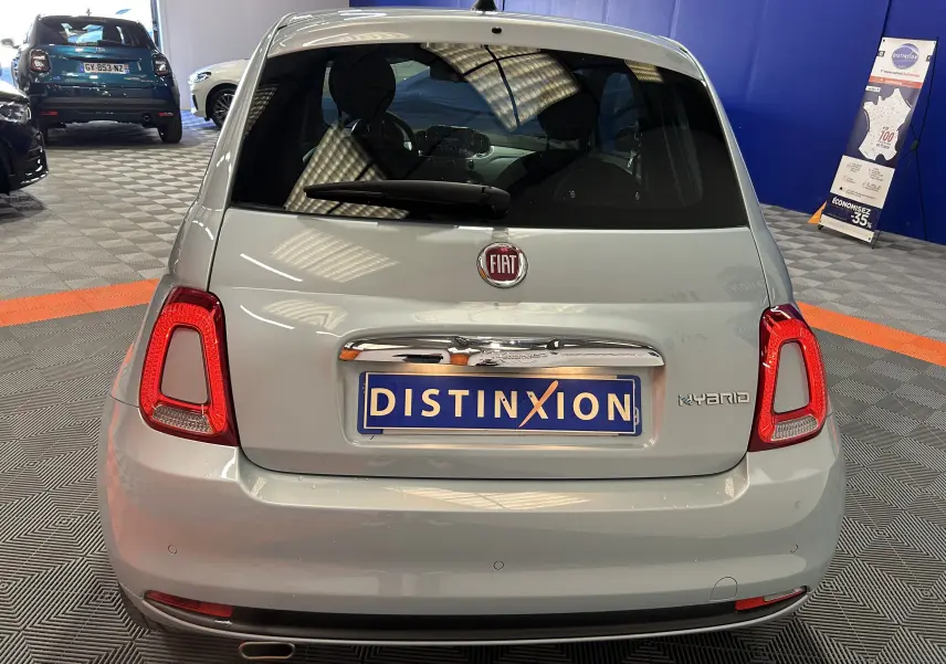 Vue arrière d'une FIAT 500 hybride couleur vert clair Rugiada, avec feux arrière allumés et plaque Distinxion visible en intérieur showroom.