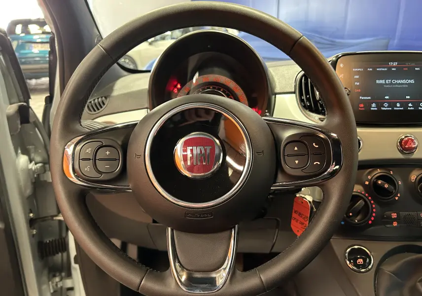 Vue intérieure centrée sur le volant noir du Fiat 500 2023 avec tableau de bord et écran tactile en arrière-plan.