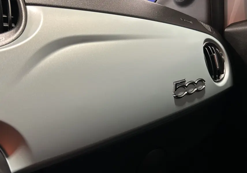Vue rapprochée de la planche de bord Rugiada Green de la Fiat 500 avec logo 500 chromé et sortie d’air ronde.