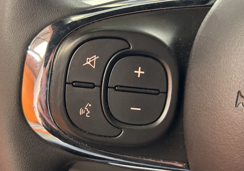 Gros plan sur les boutons de commande audio et vocales noirs sur le volant d'une FIAT 500 2023 finition Rugiada Green.