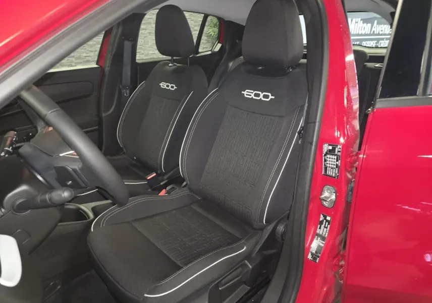 Vue intérieure côté conducteur d'une FIAT 600 rouge 2024, sièges tissu noir avec logo "600" brodé.