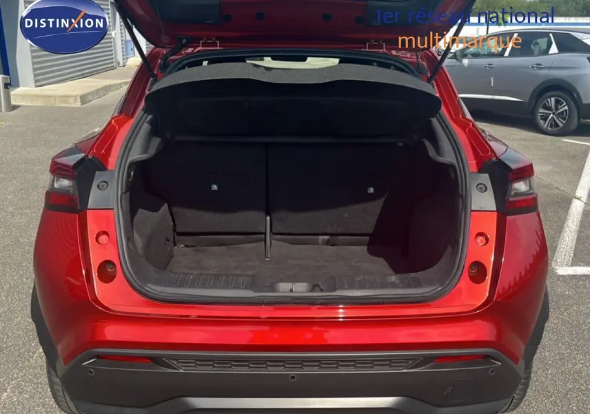Vue arrière du Nissan Juke 2024 rouge Fuji Metal avec coffre ouvert, montrant l'espace de chargement vide.