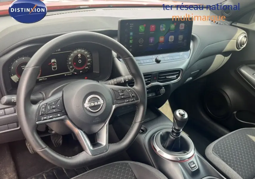 Vue intérieure du poste de conduite du Nissan Juke 2024, volant cuir et levier de vitesse manuel, écran tactile central visible.