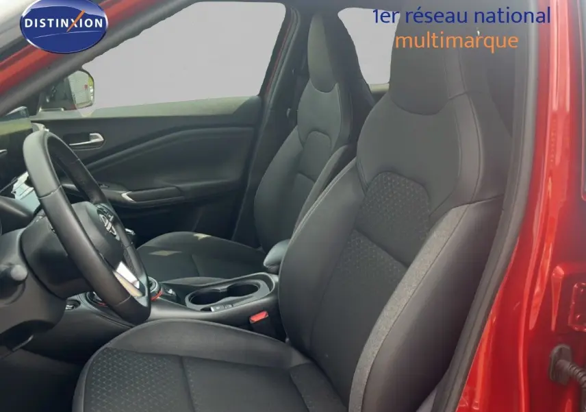 Vue intérieure côté conducteur du Nissan Juke 2024 rouge Fuji Metal, sièges tissu noir avec détails gris et volant multifonction.