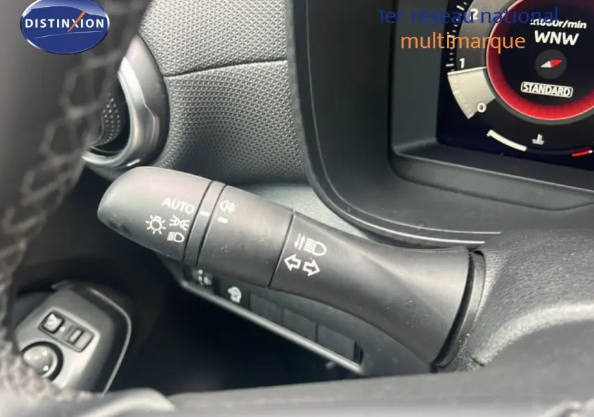 Gros plan sur la commande des phares et clignotants du tableau de bord d’un Nissan Juke rouge Fuji Metal 2024.