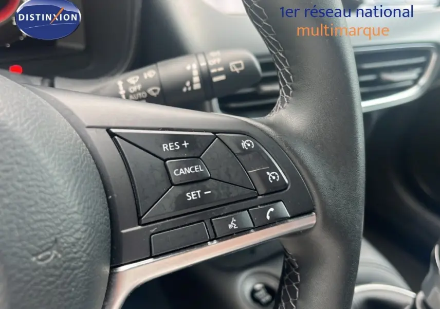 Gros plan sur les commandes de régulateur de vitesse au volant cuir noir du Nissan Juke rouge Fuji Metal 2024.
