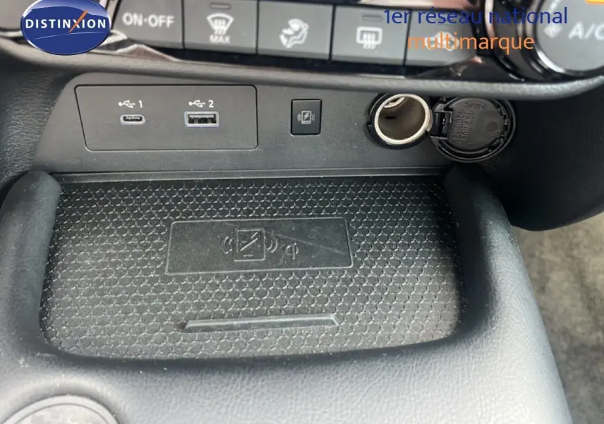 Vue rapprochée de la console centrale du Nissan Juke rouge Fuji Metal 2024, montrant ports USB, prise 12V et zone de recharge sans fil.