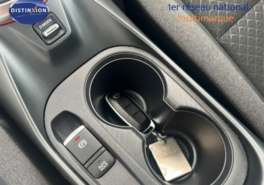 Gros plan sur la console centrale intérieure du Nissan Juke 2024, avec clé dans porte-gobelet et bouton frein à main électronique.
