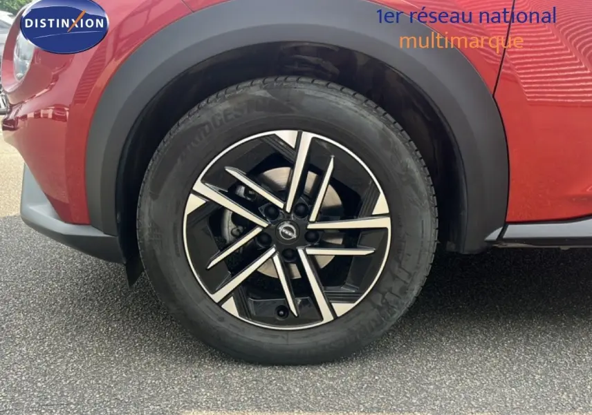 Gros plan sur la roue avant gauche du Nissan Juke rouge Fuji Metal avec jante alliage noire et argentée.