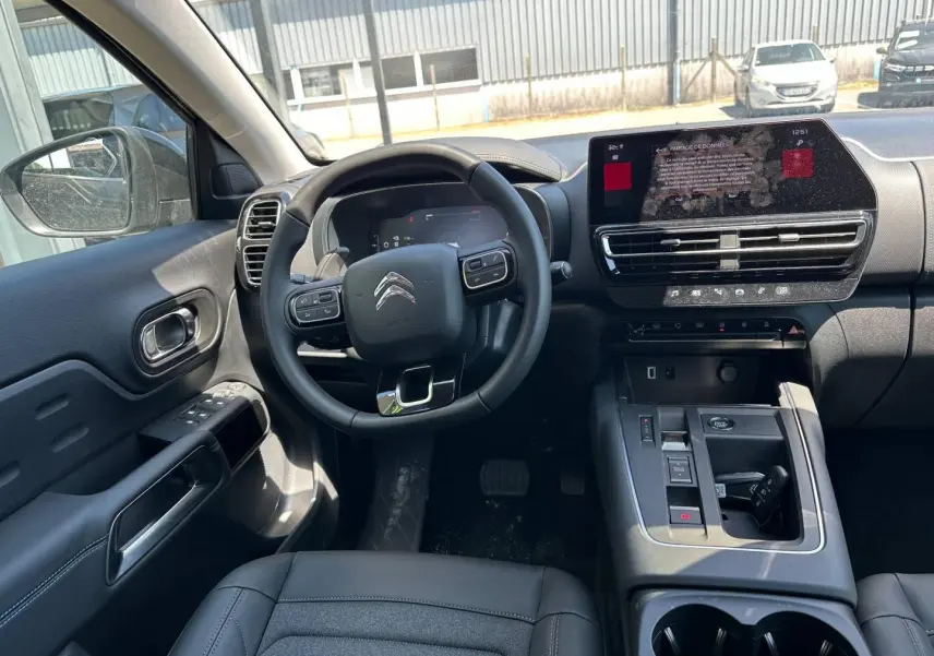 Vue intérieure du poste de conduite du Citroën C5 Aircross 2025, volant cuir noir et écran tactile central.