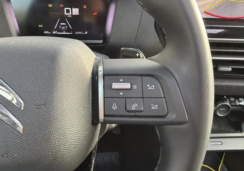 Gros plan sur le volant cuir de la Citroën C4 2024 avec commandes audio et combiné numérique en arrière-plan.