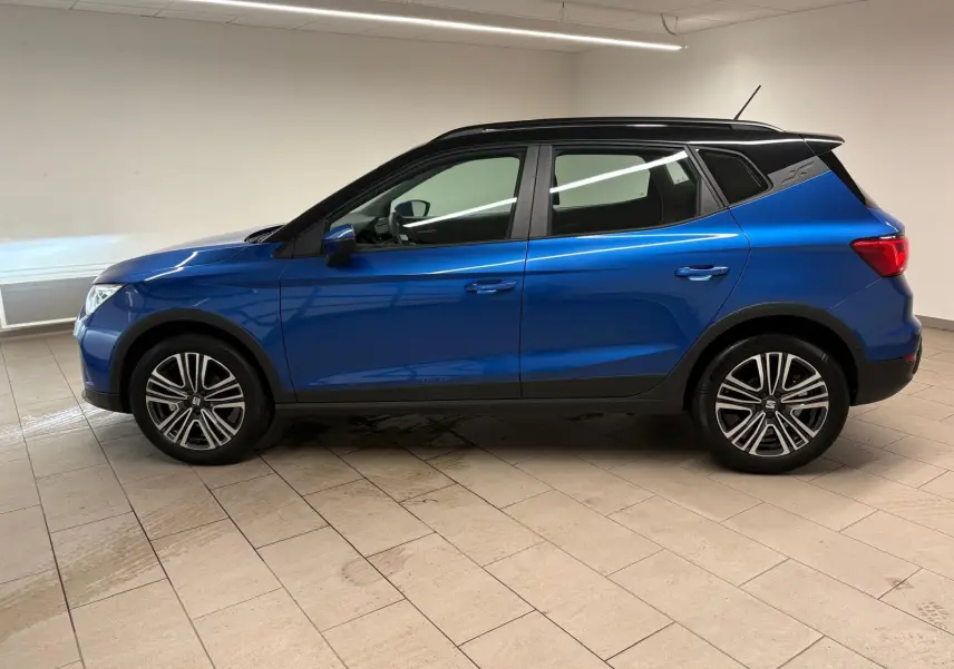 Vue de profil côté gauche du SEAT Arona 2025 en bleu saphir avec toit noir, soulignant ses jantes et lignes modernes.