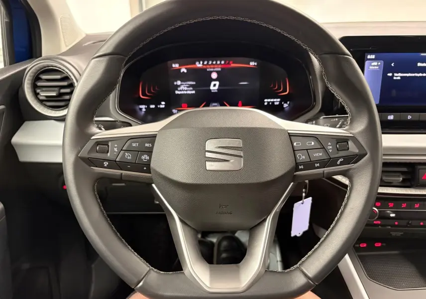 Vue rapprochée du volant multifonction noir du SEAT Arona 2025 avec tableau de bord numérique en arrière-plan.