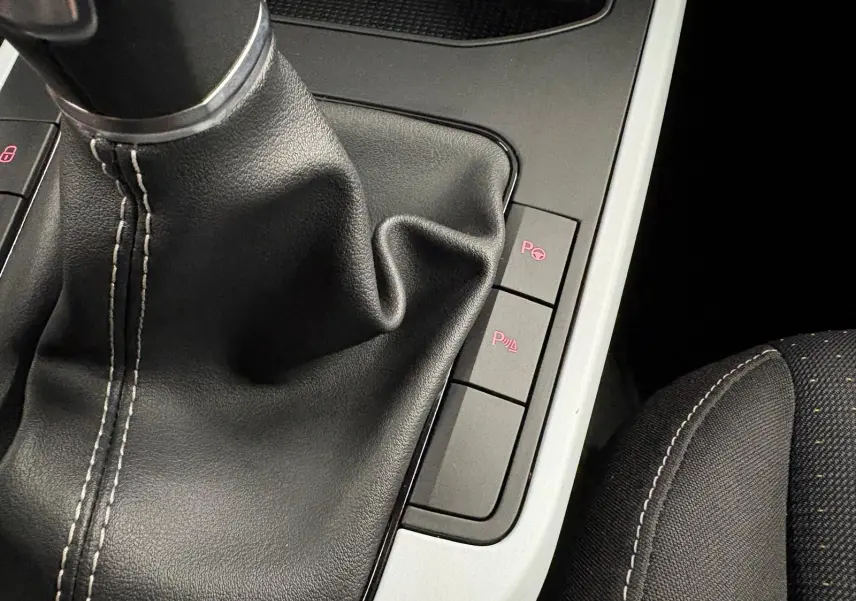 Gros plan sur la console centrale du SEAT Arona 2025, montrant le soufflet de levier de vitesses noir et les boutons de stationnement assisté.