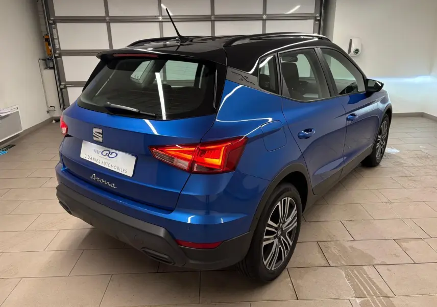 Vue 3/4 arrière droite d'un SEAT Arona bleu saphir avec toit noir, feux arrière allumés en intérieur.