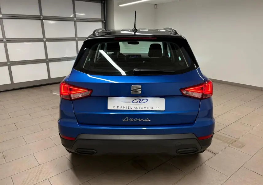Vue arrière d'un SEAT Arona 2025 bleu saphir avec toit noir, dans un intérieur neutre et éclairé.