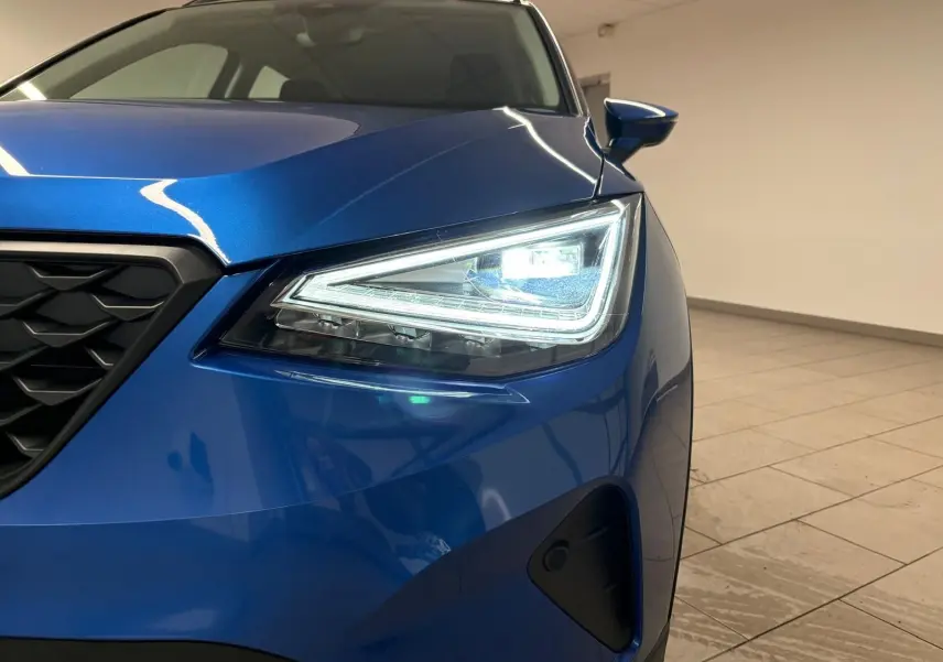 Gros plan sur l'avant droit du SEAT Arona 2025 bleu saphir avec phare LED allumé et calandre noire.