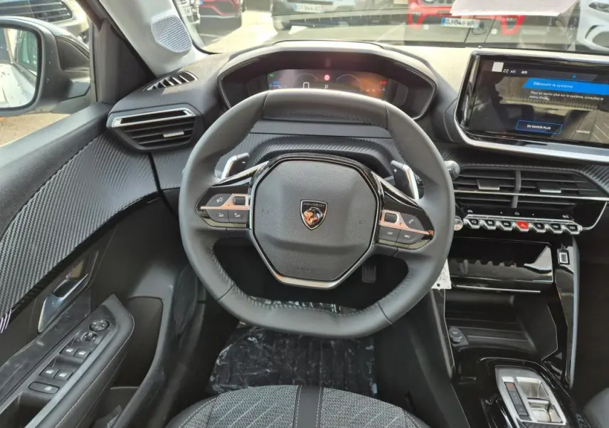 Vue intérieure centrée sur le volant cuir noir et le cockpit numérique de la Peugeot 208 Hybrid 110 Allure 2025.