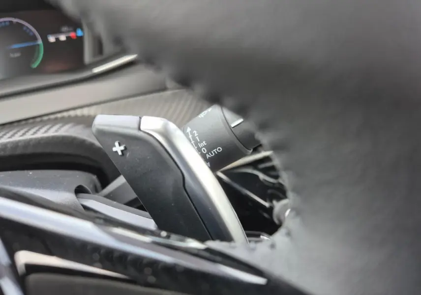 Gros plan sur la palette de changement de vitesse droite du volant d’une Peugeot 208 Hybrid blanche, tableau de bord en arrière-plan.