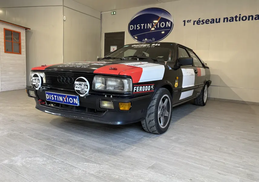 Audi Coupé GT 1983 noir vue 3/4 avant avec stickers rallye rouges et blancs, phares additionnels Hella, pneus semi-slicks.