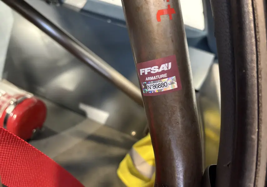 Gros plan intérieur sur l'arceau de sécurité avec autocollant FFSA et extincteur rouge dans un Audi Coupé GT noir de 1983.