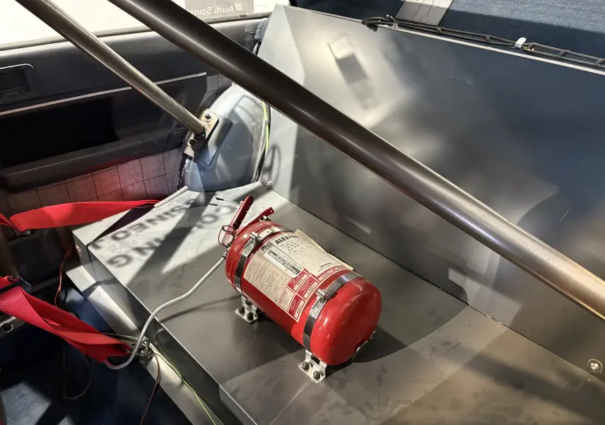 Gros plan intérieur arrière droit de l'Audi Coupé GT noir de 1983 avec extincteur rouge et arceau de sécurité visible.