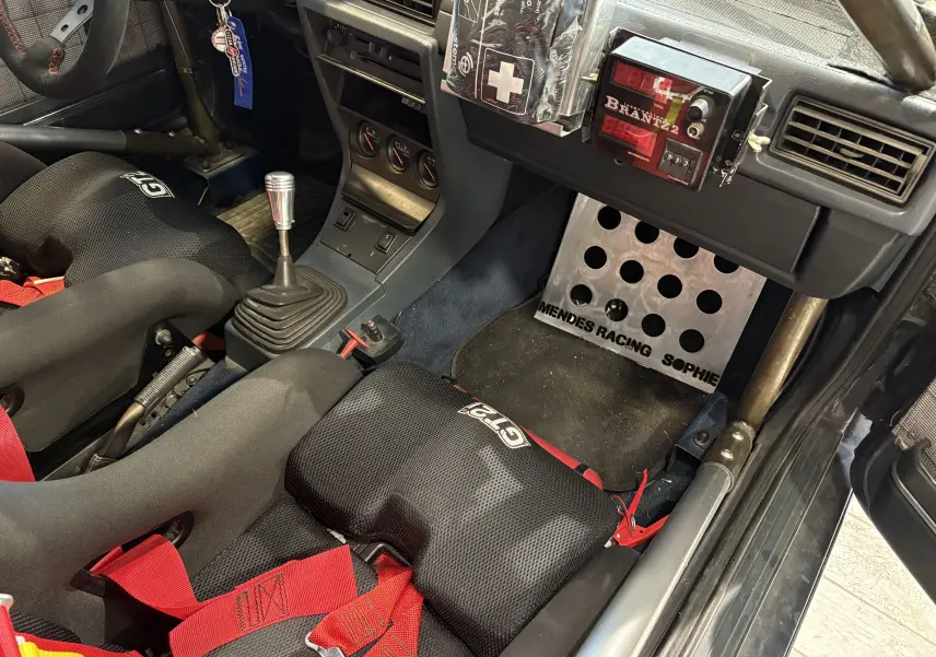 Intérieur de l'Audi Coupé GT noir vu côté passager, sièges baquets GT2i avec harnais rouge et tableau de bord rallye.