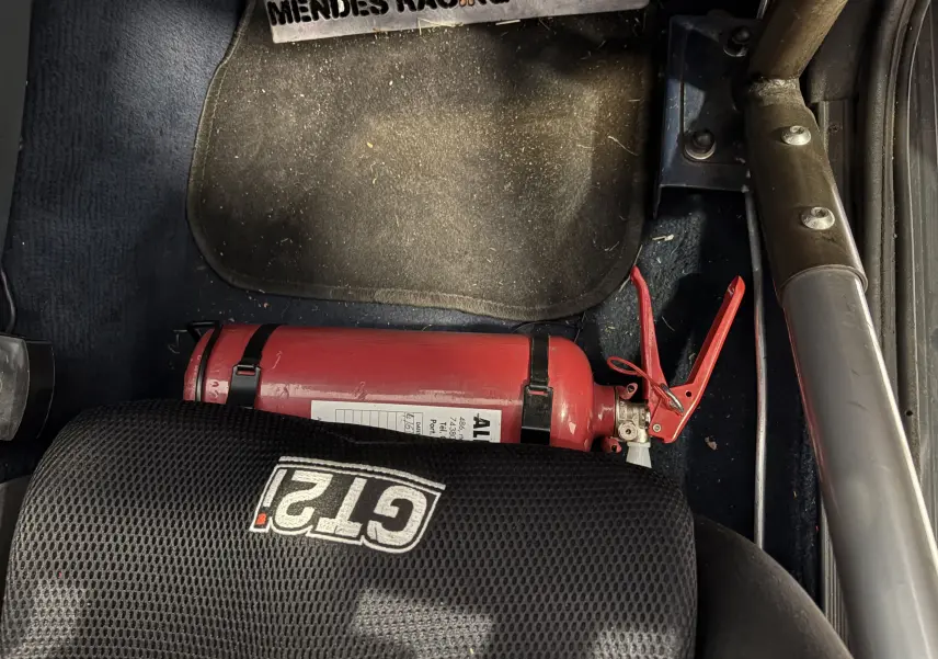 Extincteur rouge fixé au sol côté droit d'un Audi Coupé GT 1983 avec siège GT2i noir et arceau de sécurité.