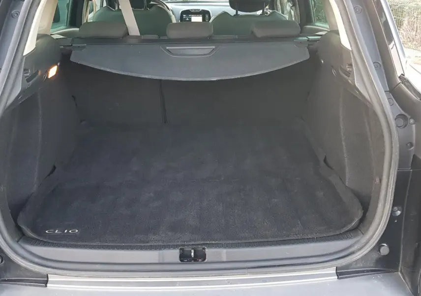 Coffre ouvert d'une Renault Clio IV Estate noire, vue arrière montrant l'espace de chargement avec tapis marqué Clio.