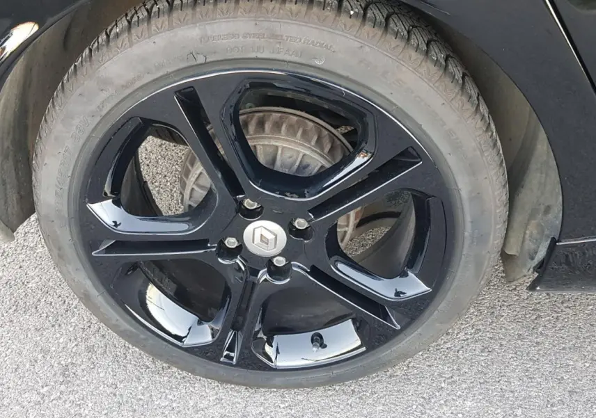 Gros plan sur la jante alliage noire de 17 pouces d'une Renault Clio IV Estate TCe 120 GT EDC noire.