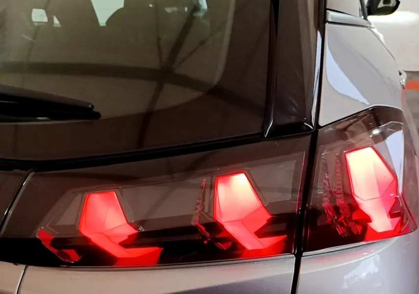 Gros plan sur les feux arrière allumés du côté gauche d’un Peugeot 2008 gris clair, vue arrière rapprochée.