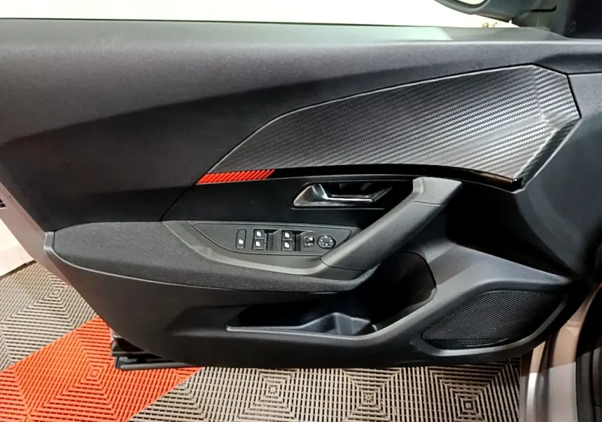 Vue intérieure côté gauche de la porte avant gris clair du Peugeot 2008 avec insert effet carbone et bande rouge décorative.