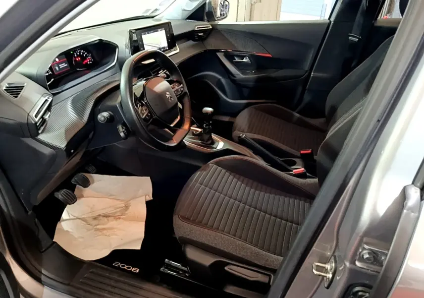 Vue intérieure côté conducteur du Peugeot 2008 gris clair, avec volant cuir, tableau de bord numérique et sièges tissu noirs.