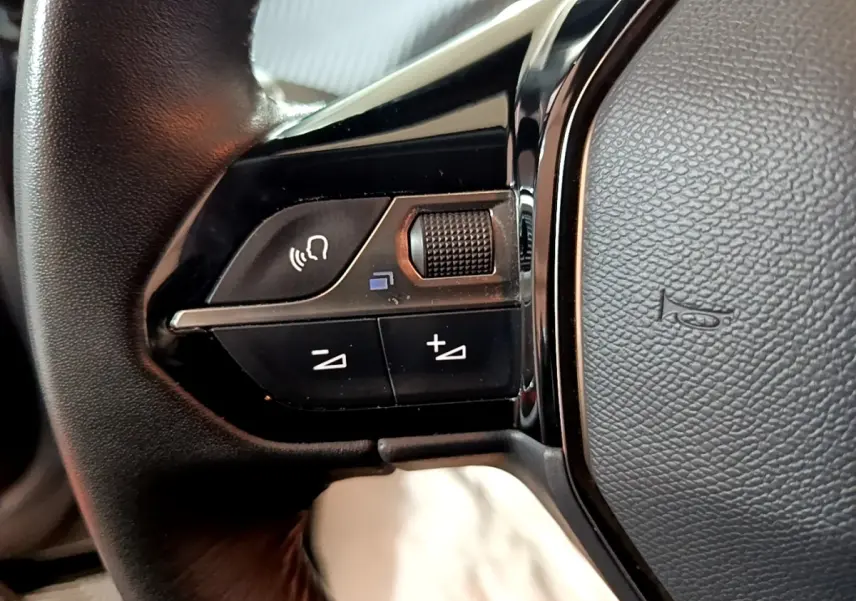 Gros plan sur les commandes vocales et volume au volant cuir côté gauche d’un Peugeot 2008 gris clair 2021.