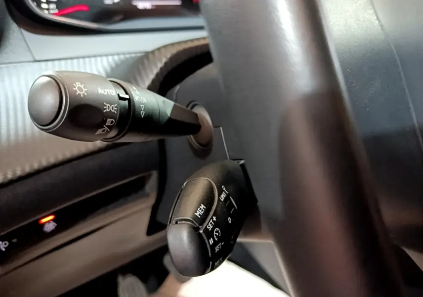 Gros plan sur les commandes au volant du Peugeot 2008 gris clair, montrant les leviers de clignotants et régulateur de vitesse.