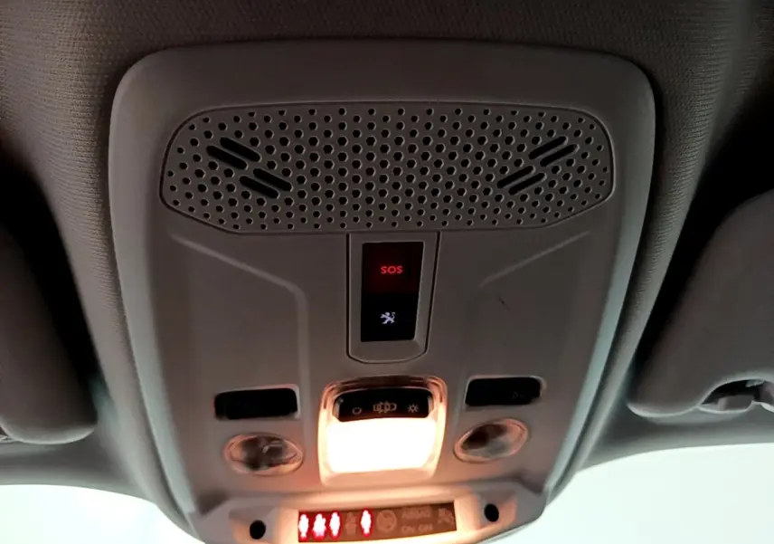 Vue en contre-plongée du plafonnier gris clair du Peugeot 2008 avec bouton SOS et éclairage intérieur allumé.