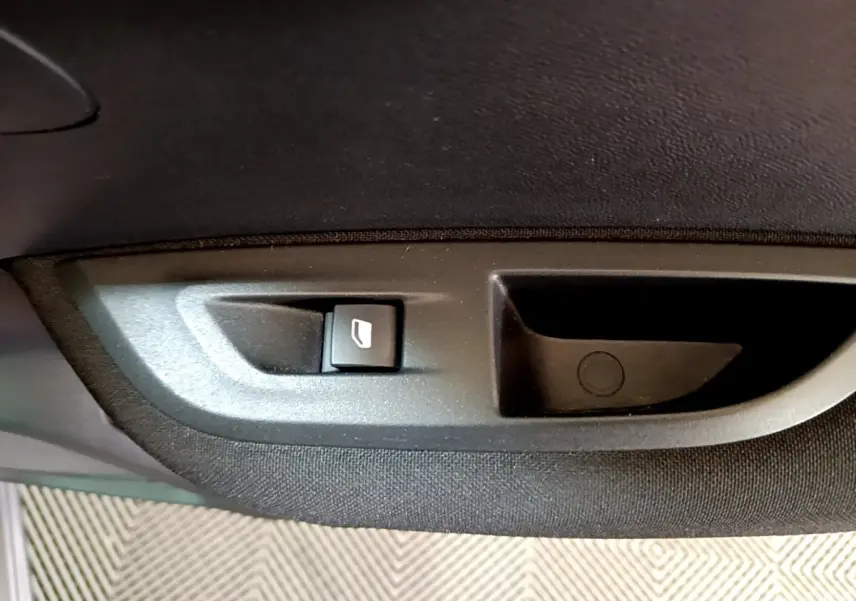 Bouton de commande de lève-vitre sur la porte intérieure côté gauche d’un Peugeot 2008 gris clair.