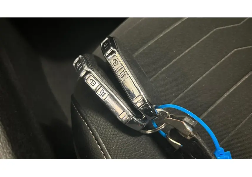 Gros plan sur deux clés de voiture KIA posées sur un siège en tissu noir à coutures blanches.