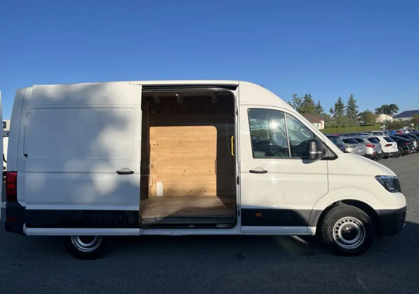 Vue latérale droite d'un Volkswagen Crafter blanc avec porte coulissante ouverte révélant l'espace de chargement en bois.