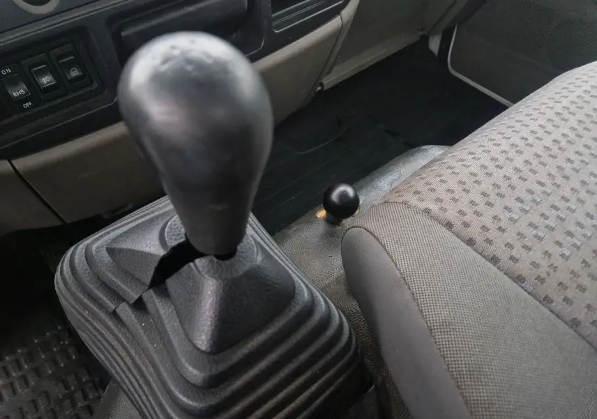 Gros plan sur le levier de vitesses manuel et siège tissu gris à motifs à l'intérieur du Nissan Cabstar blanc de 2010.