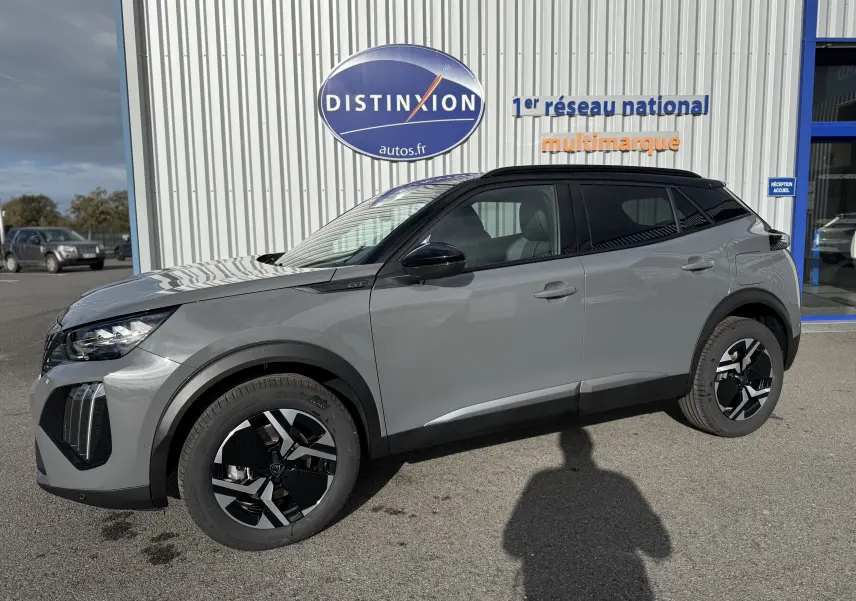 Peugeot 2008 Hybrid 145ch GT gris selenium avec toit noir, vue de profil côté gauche en extérieur devant un bâtiment.
