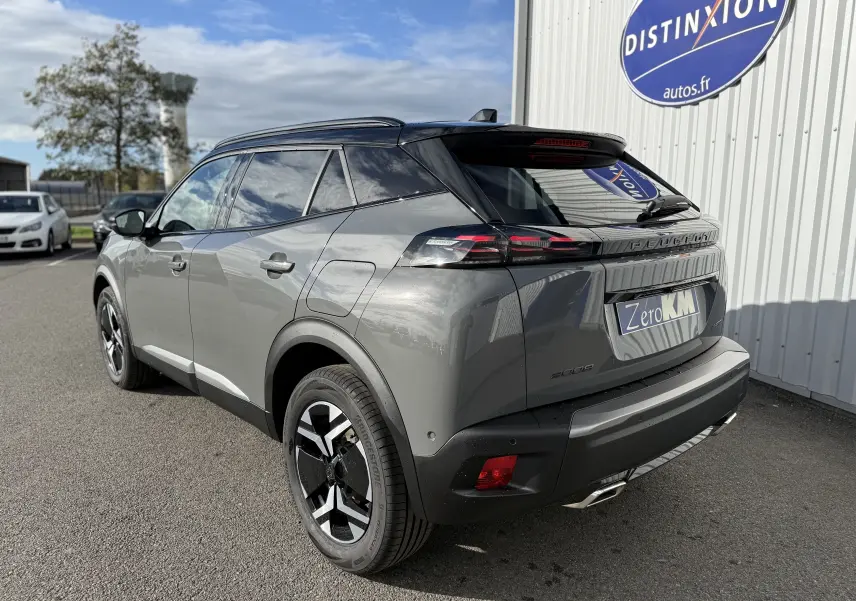 Vue 3/4 arrière droite du Peugeot 2008 Hybrid gris selenium avec toit noir et jantes distinctives, stationné devant un bâtiment.