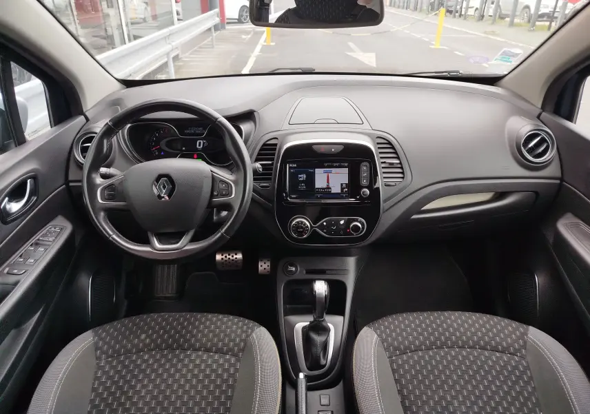 Vue intérieure avant du Renault Captur 2018 montrant le volant, la console centrale avec écran tactile et les sièges gris à motifs.