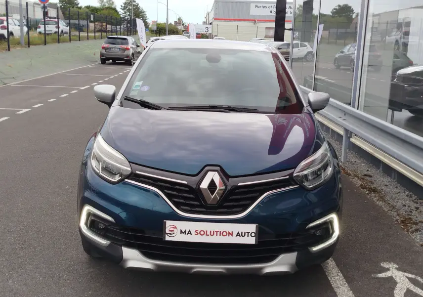 Vue avant d'un Renault Captur 2018 bleu marine fumé avec calandre noire et feux LED allumés, stationné devant un showroom.