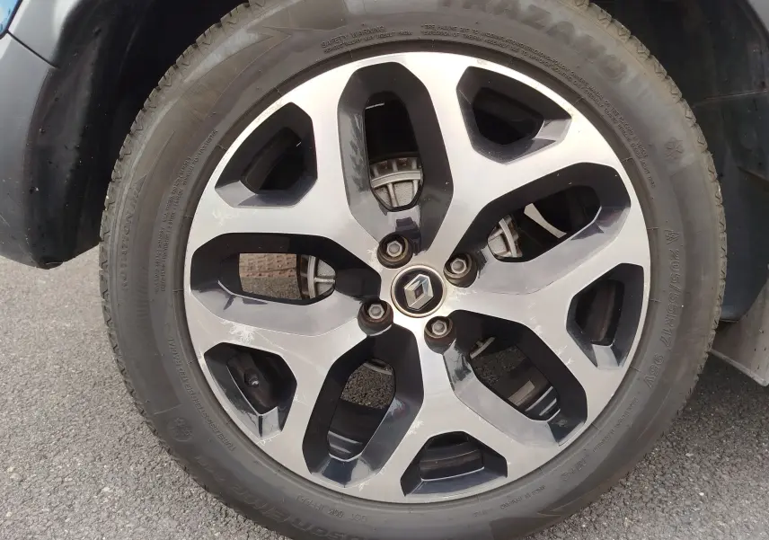 Gros plan sur la jante alliage bi-ton noire et argent du Renault Captur bleu marine fumé, roue avant gauche visible.