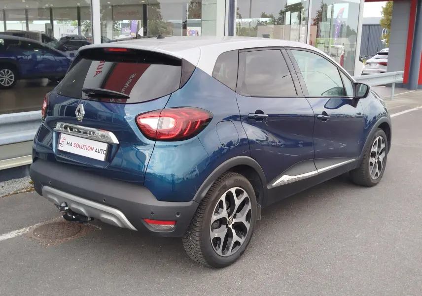 Renault Captur 2018 bleu marine fumé avec toit gris platine, vue 3/4 arrière droit, jantes bi-ton et attelage visible.