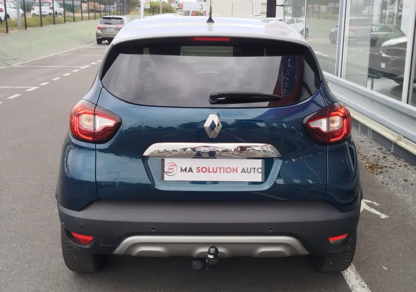 Vue arrière d'un Renault Captur bleu marine fumé avec hayon fermé et feux arrière allumés, stationné en extérieur.