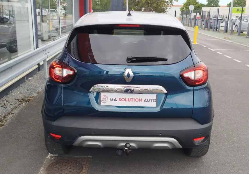 Vue arrière d'un Renault Captur bleu marine fumé avec toit gris platine, feux allumés et attelage visible.