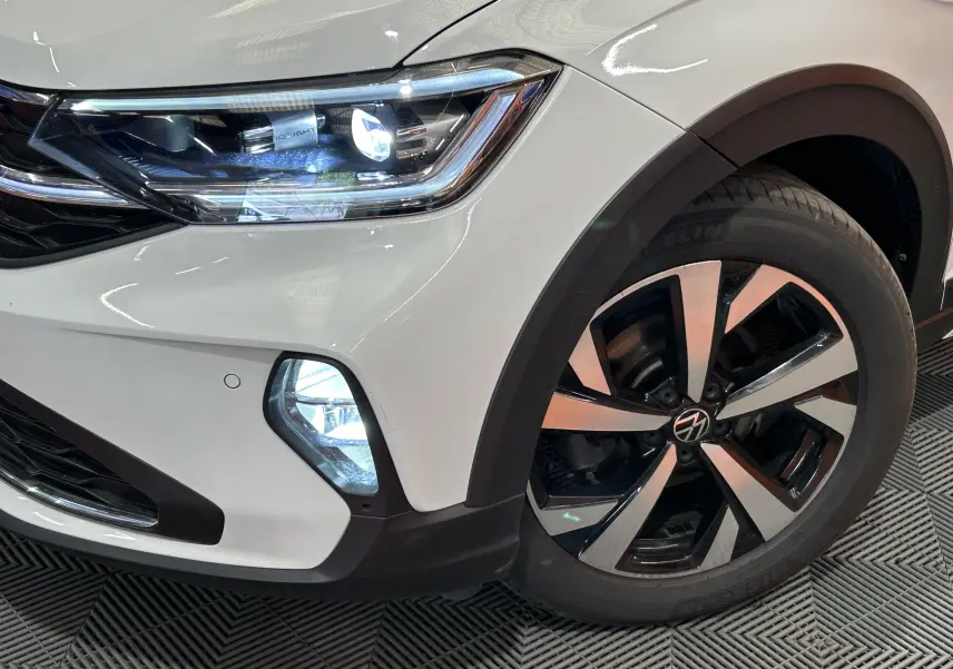 Gros plan sur l'avant droit blanc pur du Volkswagen Taigo TSI 110 DSG7 Style, mettant en valeur le phare LED et la jante alliage.