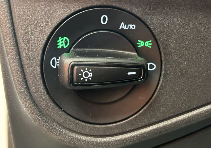 Gros plan sur le bouton de commande des phares du Volkswagen Taigo blanc, avec indicateurs lumineux verts allumés.